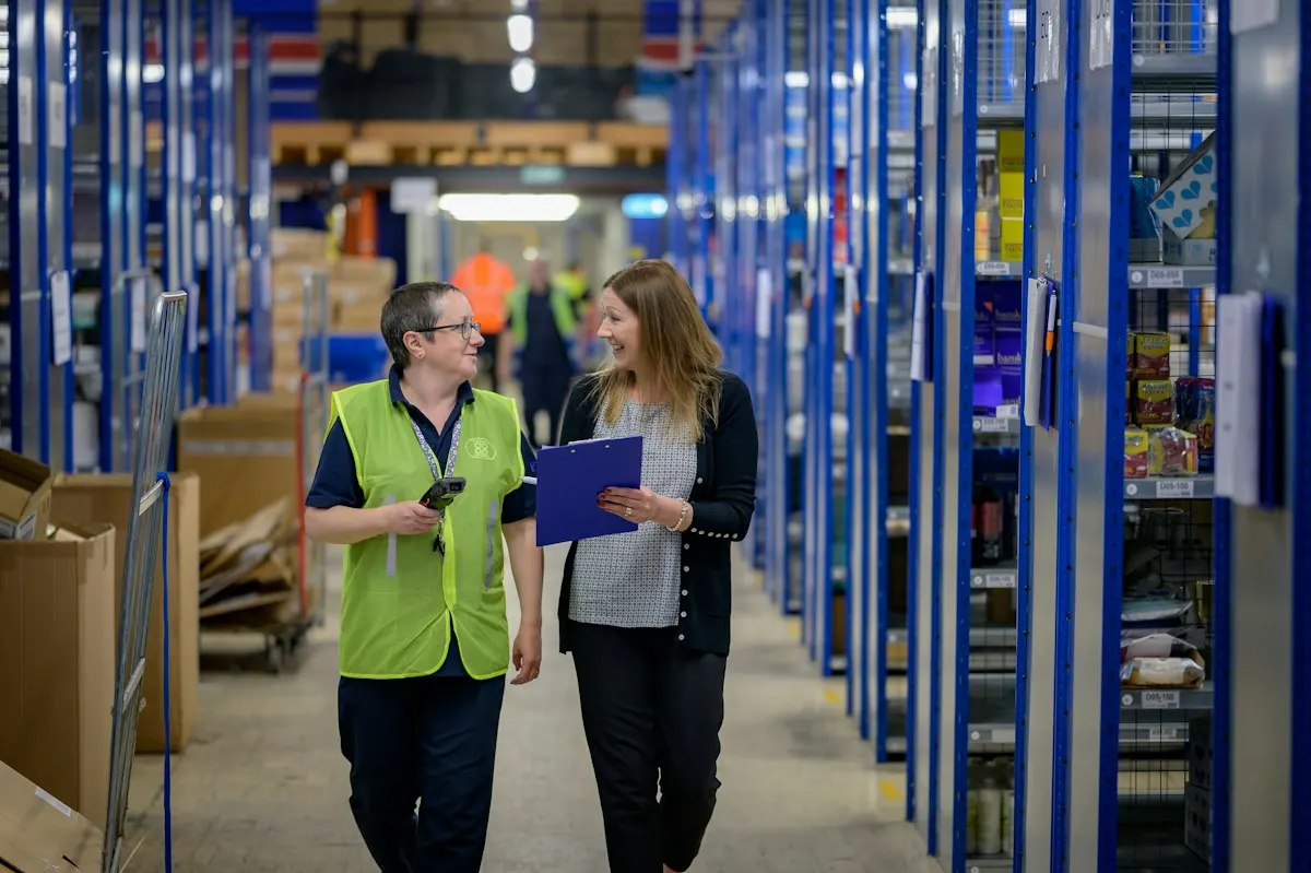 Warehouse staff discussing work beside storage racks